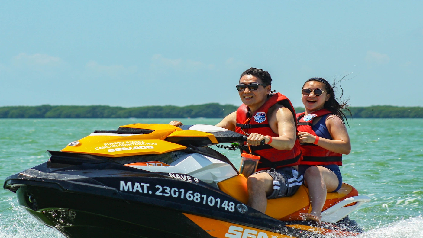 A happy couple rides a jet ski rented at Jet Ski Cancun at top speed through the Nihupte Lagoon.